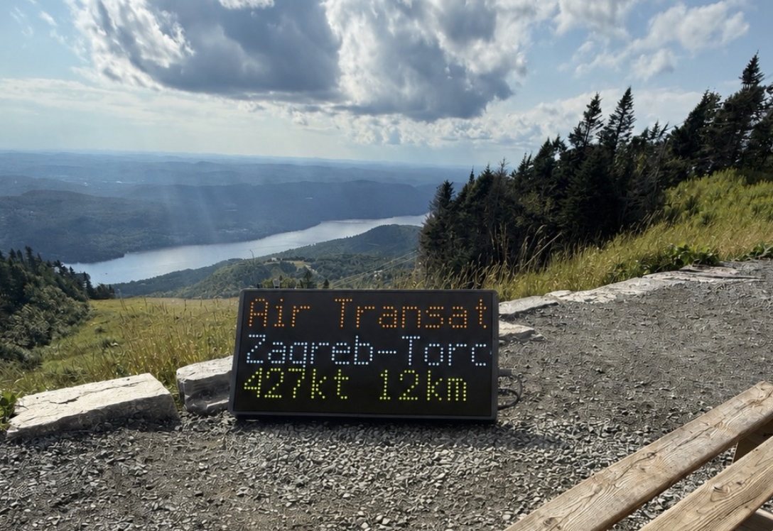 NearestPlane display outdoors on a mountainside above a lake, showing an Air Transat flight from Zagreb to Toronto at 427 knots, 12 km away
