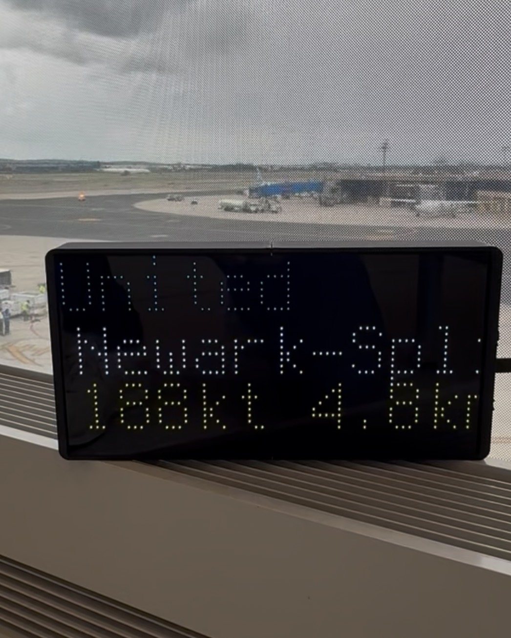 NearestPlane display on an airport window ledge overlooking the apron, showing a United flight out of Newark