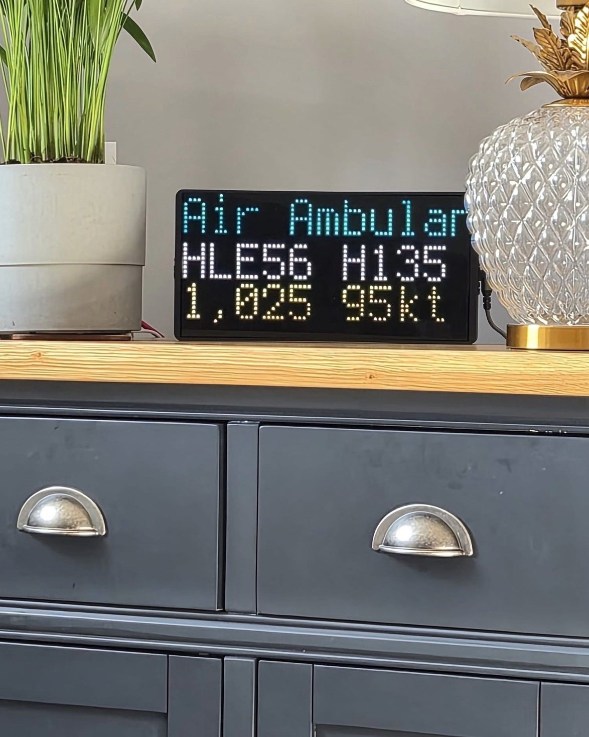 NearestPlane display on a sideboard between a plant and a lamp, naming an air ambulance helicopter overhead at 1,025 feet