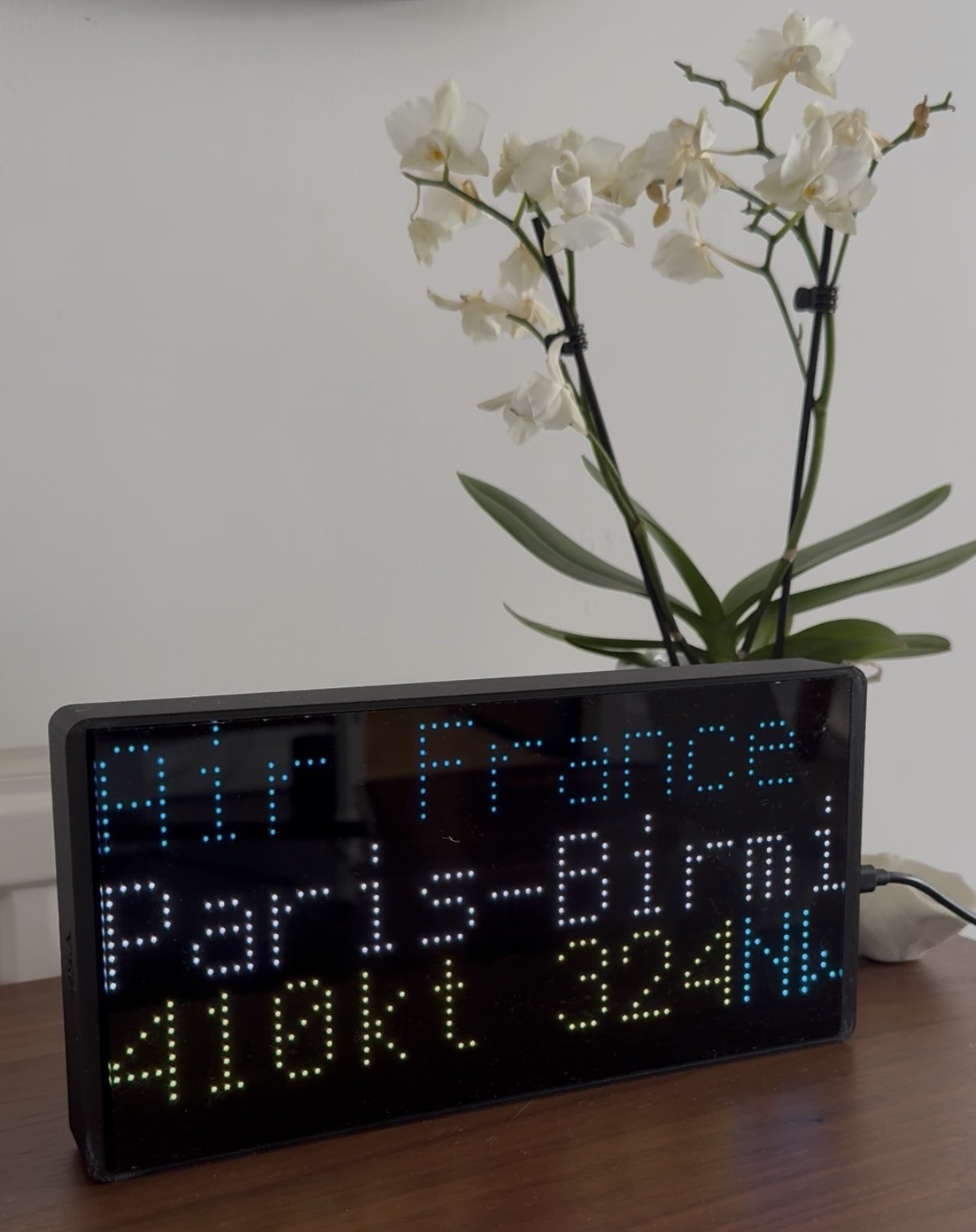 A NearestPlane display on a wooden sideboard beside an orchid, showing an Air France flight from Paris to Birmingham